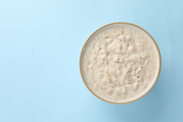 Tasty boiled oatmeal in bowl on light blue table, top view. Space for text
