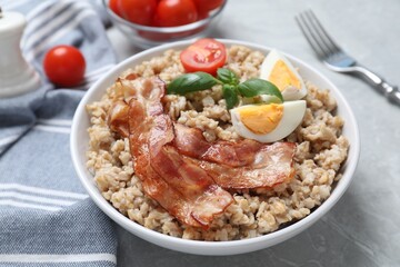 Tasty boiled oatmeal with egg, bacon and tomatoes served on light grey table, closeup