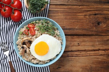 Tasty boiled oatmeal with fried egg, mushrooms and tomatoes served on wooden table, top view. Space for text