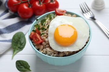 Tasty boiled oatmeal with fried egg, tomato and microgreens served on white wooden table, closeup