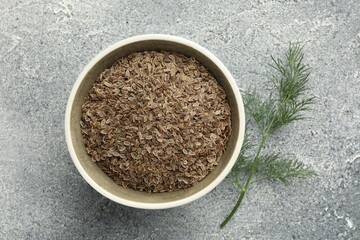 Bowl of dry seeds and fresh dill on grey table, flat lay