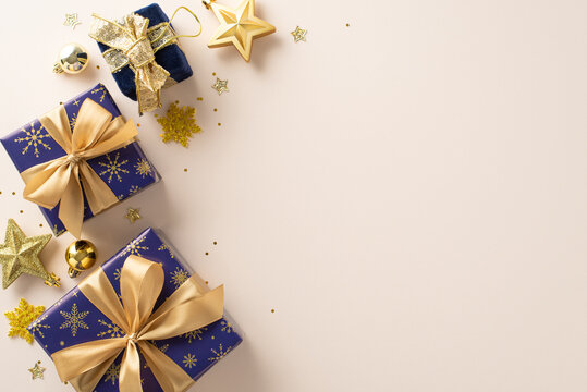 The magic of giving. Top view photograph featuring shimmering blue and gold-wrapped gifts, baubles, star embellishments, confetti, and snowflakes on a neutral background with space for your text