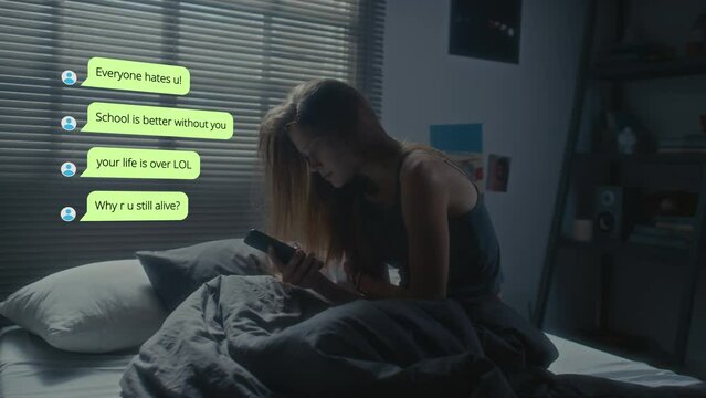 Schoolgirl siting on bed in dark room and reading humiliating messages on phone from online haters during night. CG animated text shown in copy space