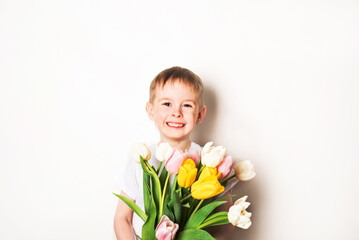 Portrait of a happy boy with freckles in a white t-shirt with a bouquet of tulips on a white background. The concept of spring, holiday, joy, life.