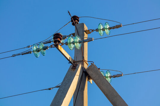 Overhead power line with wires and insulators on a concrete pole close-up on a sunny day against a blue sky