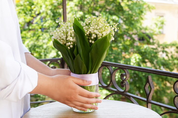 Bouquet of fresh spring flowers of  lily of the valley. Woman hands holding bouquet, placing in...