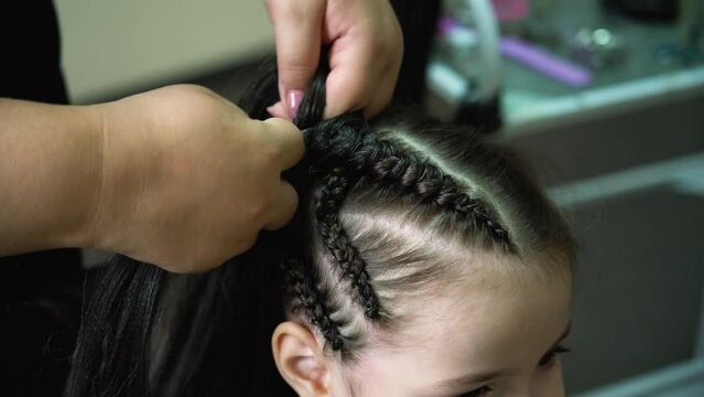 A hairdresser weaves Kanekalon into a girl's hair. Boxer braids, afro braids.
