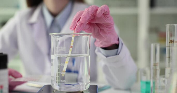 Scientist holds neutral litmus paper on test tube with sample of natural drinking water in laboratory. Checking quality of water purity