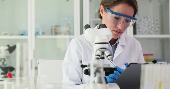 Scientist looks through a microscope and writes down information about an experiment or research in laboratory. Chemical experiments