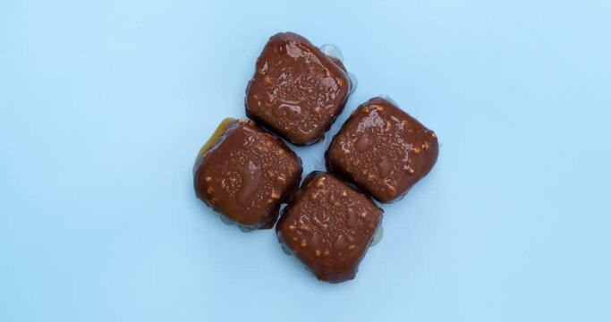 4K footage Time lapse Close-up Top view, Chocolate popsicles coated with almonds are melting on a blue background.