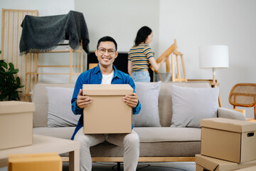 Young couple with big boxes moving into a new house, new apartment for couple, young asian man and woman helping to lift boxes on sofa for the new home, Moving house..