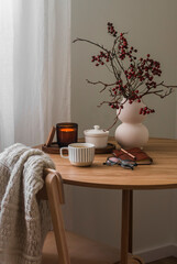 Cozy evening - cranberry branches in a vase, a lit candle, a cup of tea, a notebook on a round wooden table in the living room