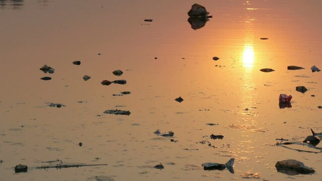 Rubbish floats down a river at sunset in Agra, pollution and waste problem in India
