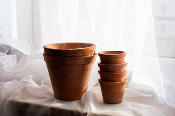 Untreated clay pots. Orange color. Autumn mood. Against the background of a delicate white curtain. Daylight. Natural color.