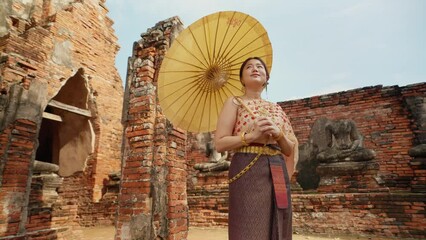 Young beautiful Asian woman wearing thai traditional dress holding umbrella in hand walking at ancient temple with old pagoda in Wat Chai Wattanaram Ayutthaya, Thailand