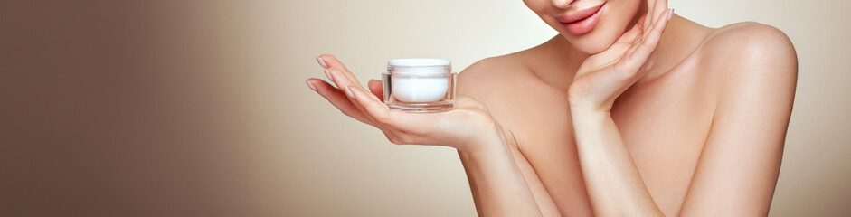 Beauty woman applying cream on her face. Young woman with clean fresh skin. Model with a jar of...