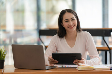 An Asian businesswoman using a digital tablet while sitting at a work desk in an office.