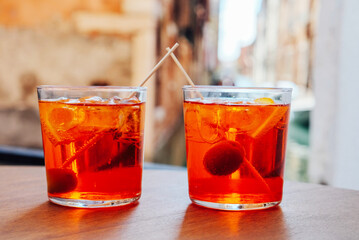 Two glasses of Aperol Spritz cocktail served near the Venetian canal. Popular italian summer aperitif drink. Venice background.