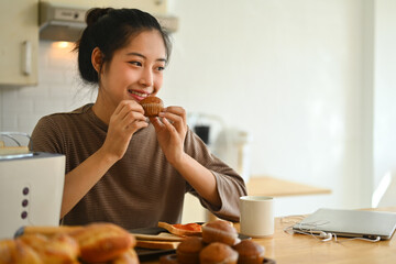 Beautiful young woman eating cupcake for breakfast in the kitchen at home