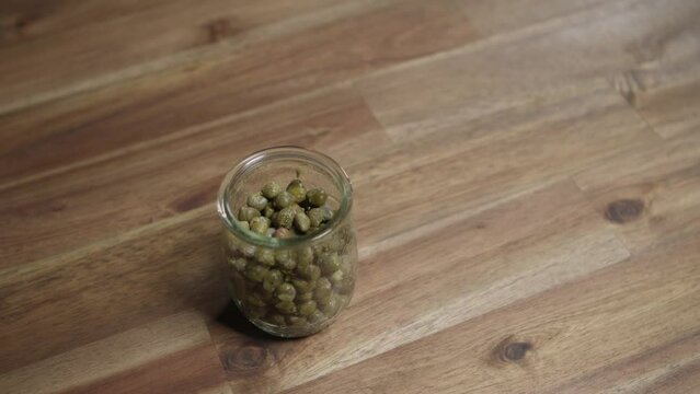 Medium close shot of caper sitting in a small glass jar. Top shot, panning. Nobody, studio.