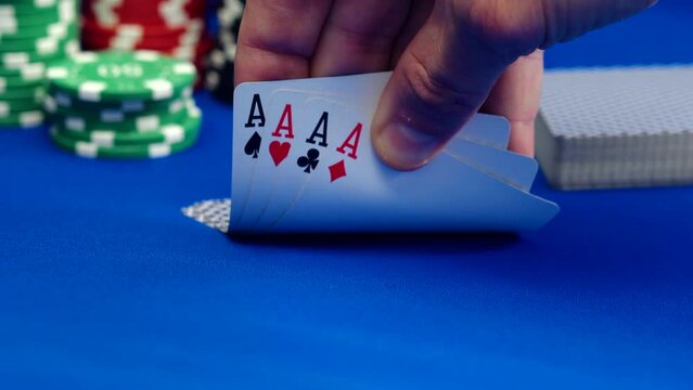 Hands of poker player betting shows cards of aces with casino chips in the background on blue table, Gambling background