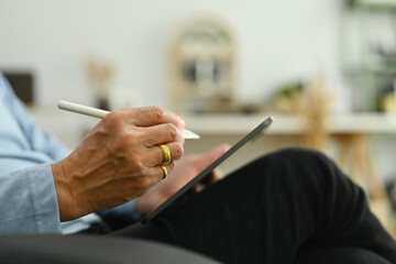 Side view of mature man sitting on sofa and using digital tablet. Retirement lifestyle and technology concept