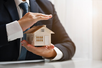 Businessman protecting house model with hands. Real estate and property Insurance concept