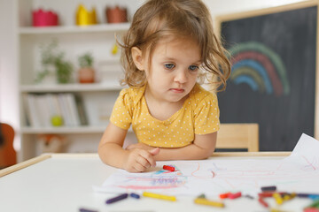 Young girl siting on the chair and drawing with colourful crayon. Home learning concept.
