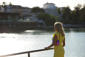 Blonde, young and beautiful woman leaning on the railing on the riverside promenade in seville...