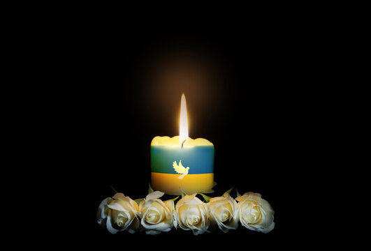 White roses with a burning candle on the dark background with ukrainian flag. Funeral flower and candle on table against black background. Funeral symbol. Mood and Condolence card concept