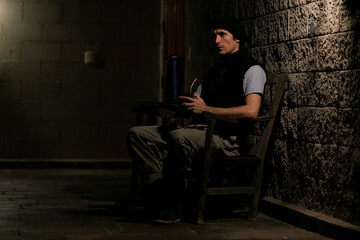 gaucho drinking mate and posing for the camera in a gallery in the light of a lantern