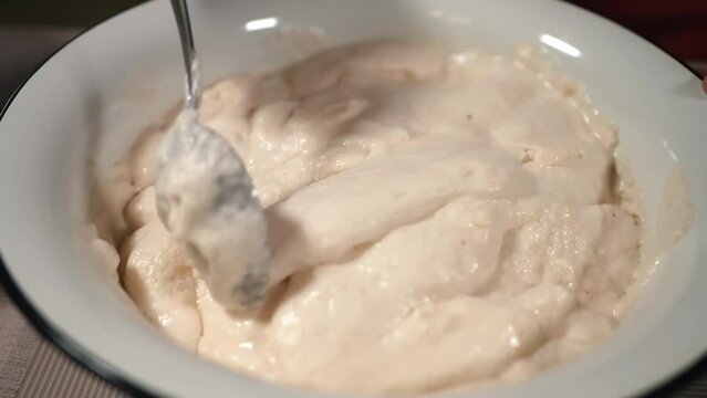 The hostess is preparing dough in the kitchen. Mixes beaten eggs with flour. Women's hands stir the mixture for preparing pascha for Easter. Baking strips of cupcakes and bakery products with raisins