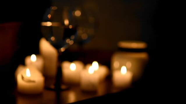 blurry background of burning candles and wine glasses in the dark. Background image for a holiday, dinner, romantic evening