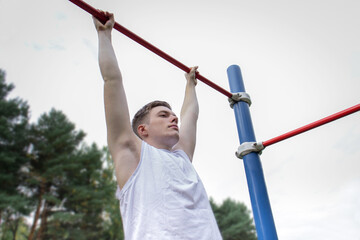 A cute young man is doing exercises on a horizontal bar at the stadium