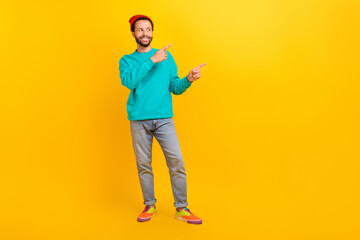 Fototapeta na wymiar Full size photo of funky guy wear teal sweatshirt red hat directing look at proposition empty space isolated on yellow color background