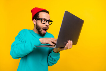Photo of impressed programmer guy wear teal sweatshirt red beanie hat staring at laptop write code...
