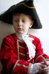 Little boy dressed in Rococo era costume in a red coat and black hat on a white background