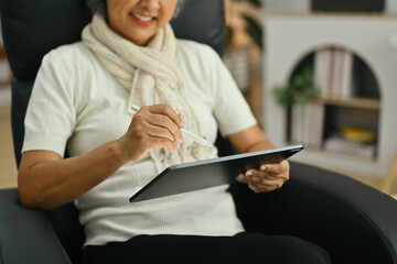 Happy middle age woman using digital tablet on comfortable armchair. People and technology concept