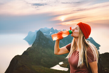 Thirsty woman drinking water with reusable plastic bottle on mountain summit girl traveling in...