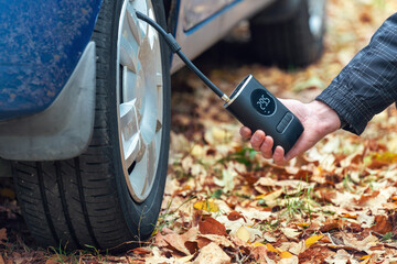 Inflating car tires with a portable wireless air pump outdoor - obrazy, fototapety, plakaty