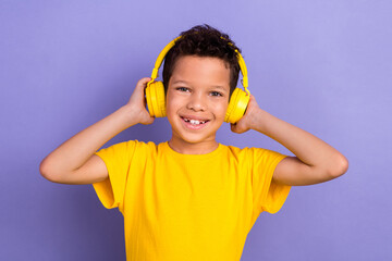 Photo portrait of nice young pupil boy touch headphones enjoy radio song dressed yellow garment isolated on violet color background