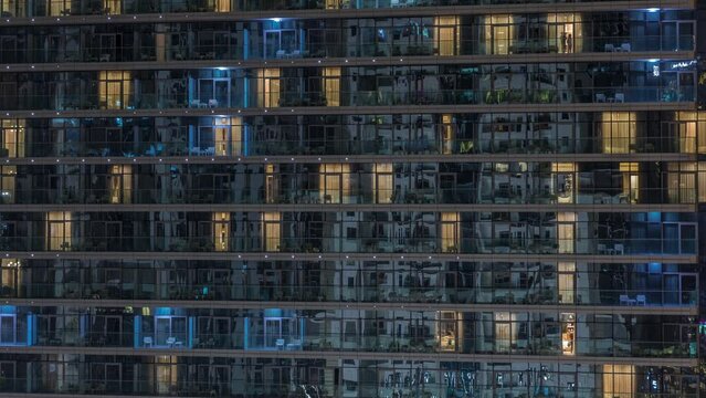 Tall blocks of flats with glowing windows located in residential district of city aerial timelapse. Evening light in rooms in towers and skyscrapers. Balconies with chairs and tables