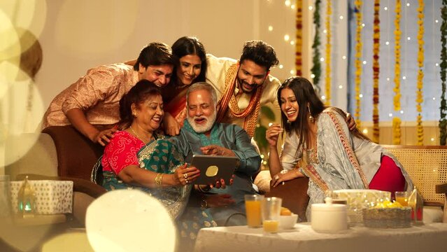 Ethnic Hindu Indian happy smiling family members sitting together and video call on ipad on the occasion of Diwali festival.well decoreted home.they are all very happy.