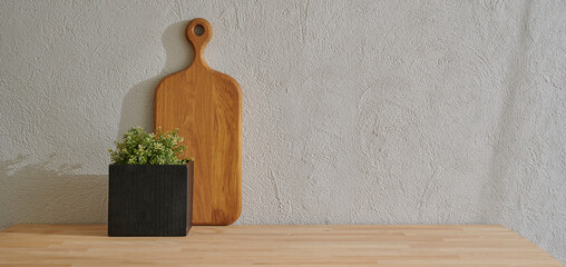 Wooden cutting board on the table, kitchenware, vase of plant grey decorative wall background.