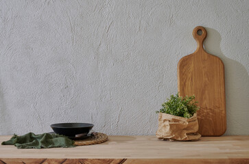 Kitchenware is on the wooden table close up, cutting board vase of plant, plate, spoon, fork, water glass.