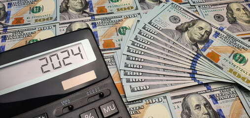 New financial year 2024. Calculator on the screen against the background of US $100 banknotes....