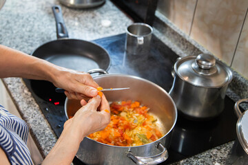Detail of a person cooking food on the electric hob with pans and cutting the food to make the...