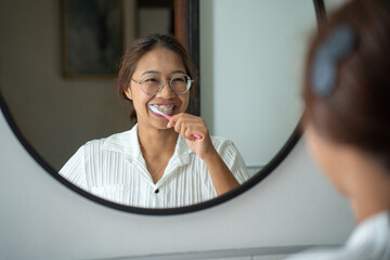 morning brushing teeth. Young woman brushing teeth with toothbrush and looking in mirror in bathroom. Oral hygiene, healthy teeth and care.