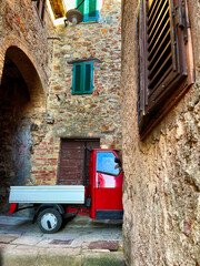 Rote italienische Ape in einer kleinen italienischen Straße, mit alten Natursteinhäusern mit Torbogen.
