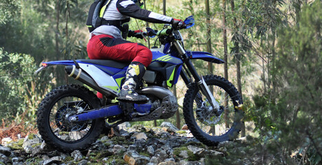 Person on a motorbike doing a mountain trail in extreme action going over a pile of rocks, off-road motorcycling hobby